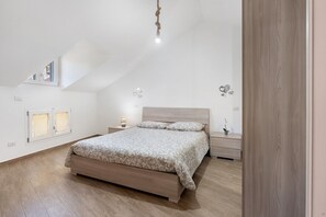 Un dormitorio con techo inclinado, una cama con colcha estampada, mesitas de noche con lámparas y una pequeña planta en maceta.
