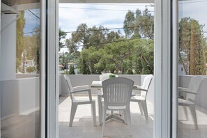 A balcony with white plastic chairs and a table, overlooking a residential area with trees and houses.