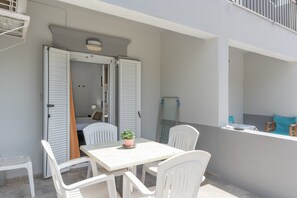 A balcony with a table and chairs, a potted plant, and a partially open door leading to a room. - Apartment 'No 10' with Shared Pool, Wi-Fi and Air Conditioning (Kalymnos)
