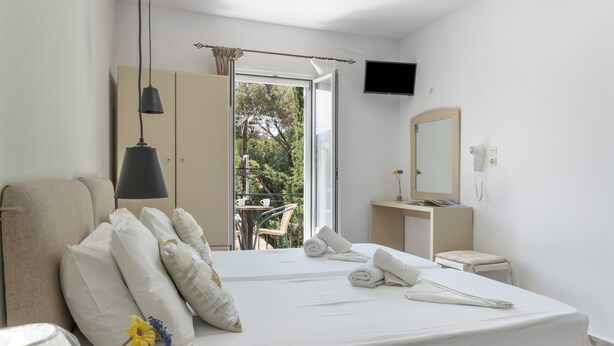 Habitación de hotel con cama, escritorio, silla, televisión y balcón con mesa y sillas.
