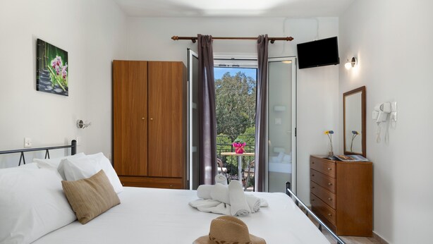 A hotel room with a bed, a wardrobe, a television, a mirror, and a balcony with a table and chairs. - Apartment 'No 12' with Shared Pool, Wi-Fi and Air Conditioning (Kalymnos)