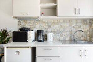 Une petite cuisine équipée d’un four à micro-ondes, d’une machine à café et d’une bouilloire sur le plan de travail, ainsi que d’un évier et d’un petit réfrigérateur.