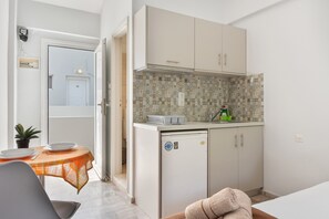 Una cucina compatta con rivestimento in piastrelle, un piccolo frigorifero e un'area pranzo con tavolo e sedie.