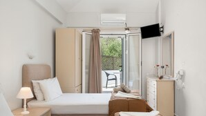 Habitación de hotel con cama, sofá, escritorio con lámpara, televisor, armario y puerta corredera a un área exterior.