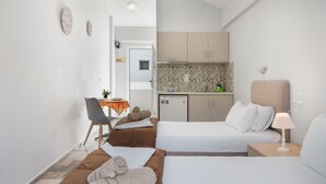 Habitación de hotel con dos camas, un escritorio, una silla, una pequeña cocina y un baño.