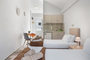 Une chambre d’hôtel avec deux lits, un bureau, une chaise, un petit coin cuisine et une salle de bain.