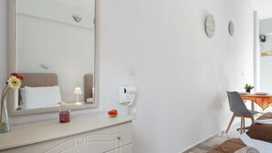 Una habitación de hotel con una cama, una mesita de noche con una lámpara, un espejo, una pequeña mesa con una planta y una silla.