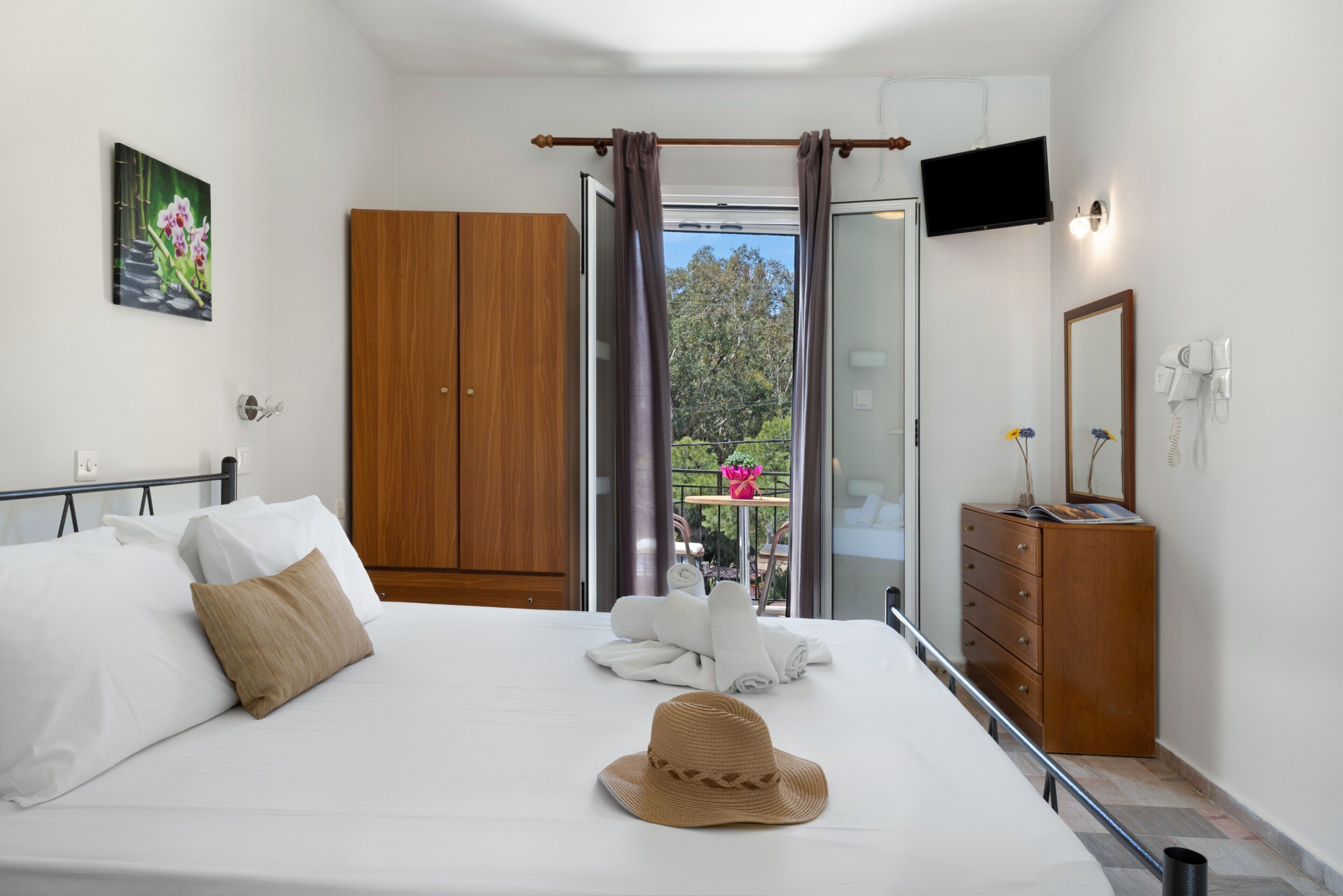 Une chambre d’hôtel comprenant un lit, une armoire, une télévision, un miroir et un balcon avec une table et des chaises.