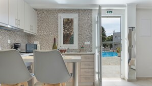 A modern kitchen with a dining area, a view of a swimming pool, and a door leading to an outdoor area. - Apartment 'No 16' with Shared Pool, Wi-Fi and Air Conditioning (Kalymnos)