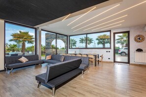 Uma sala de estar moderna com um sofá seccional, janelas amplas e uma área de jantar.