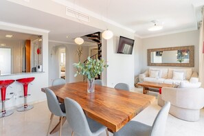 A modern dining area with a wooden table, grey upholstered chairs, and a vase with green foliage.