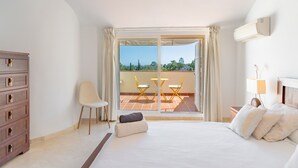 Ein Schlafzimmer mit Bett, Sessel, Nachttisch, Kommode und einem Balkon mit Blick.