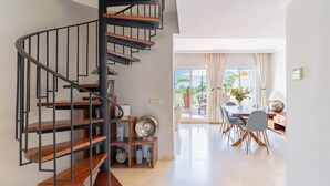 Ein modernes Interieur mit einer Wendeltreppe, einem Essbereich mit Tisch und Stühlen sowie Blick ins Freie durch eine Glastür.