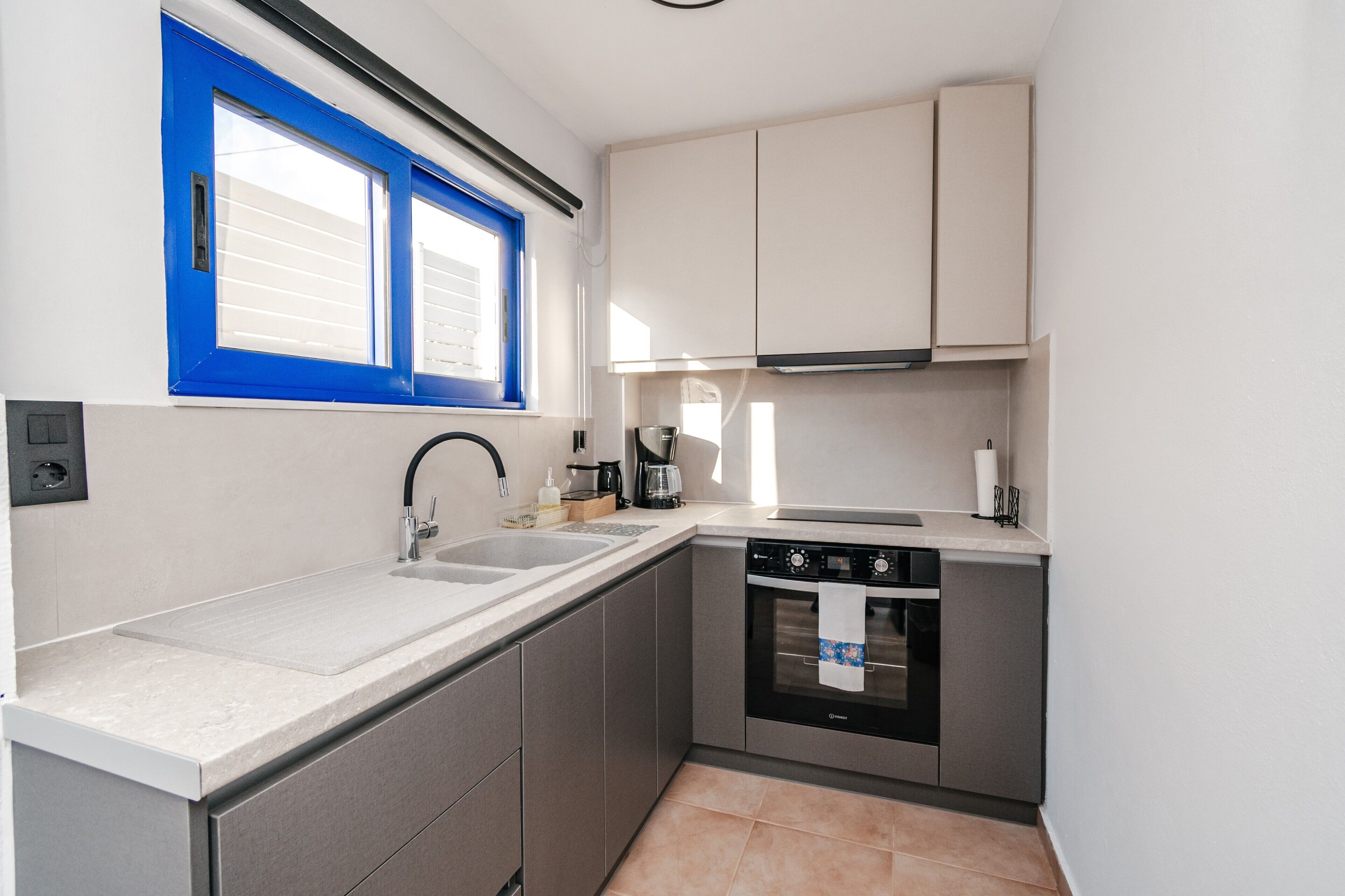 A compact kitchen with a double sink, a dishwasher, and a window with blue shutters.