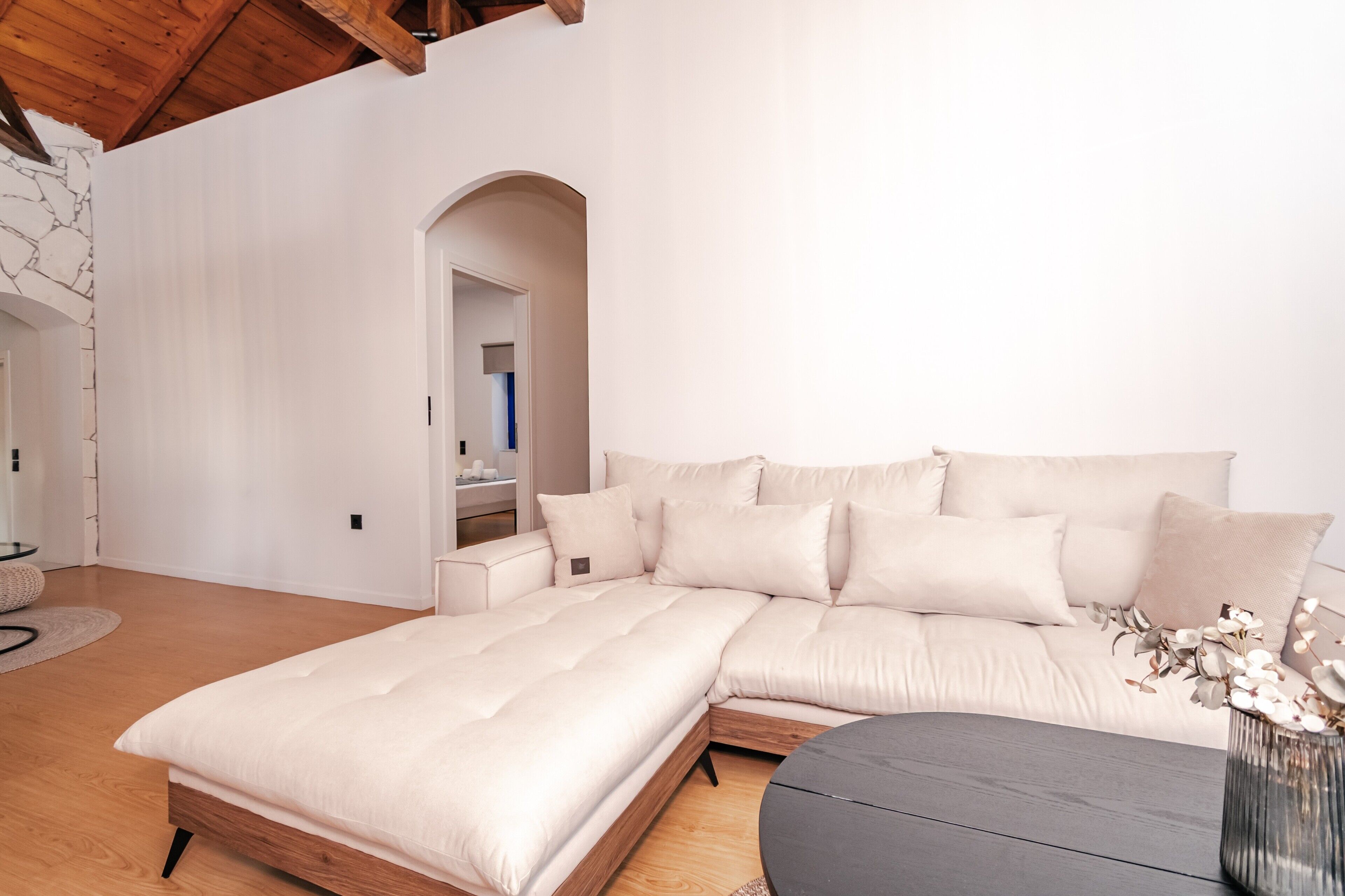 Ein modernes Schlafzimmer mit einem Bett, einem Schlafsofa, einem runden Tisch und einer Vase mit Blumen.