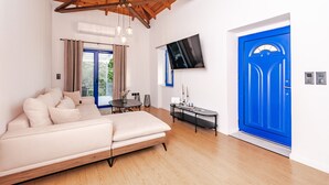 A modern living room with a wooden ceiling, a beige sofa, a TV, and a blue door. - Country House 'Navarino Baths' with Sea View, Wi-Fi and Air Conditioning (Vromonérion)