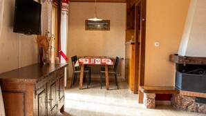 A wooden interior with a dining table, chairs, a TV mounted on the wall, and a fireplace. - Studio Apartment 'C3 - Chalet Tournier' with Mountain View, Shared Garden and Wi-Fi (Les Gets)