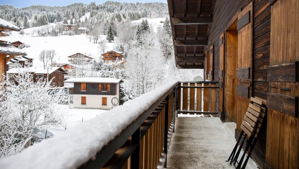 A wooden balcony with a view of a snow-covered village and mountains. - Studio Apartment 'C3 - Chalet Tournier' with Mountain View, Shared Garden and Wi-Fi (Les Gets)
