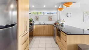 A modern kitchen with a stainless steel refrigerator, wooden cabinets, a black countertop, and orange pendant lights.