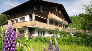 Een meerlaags chalet met een schuin dak, houten balkons en een tuin vol wilde bloemen.