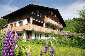 A multi-story chalet with a sloped roof, wooden balconies, and a garden with wildflowers.