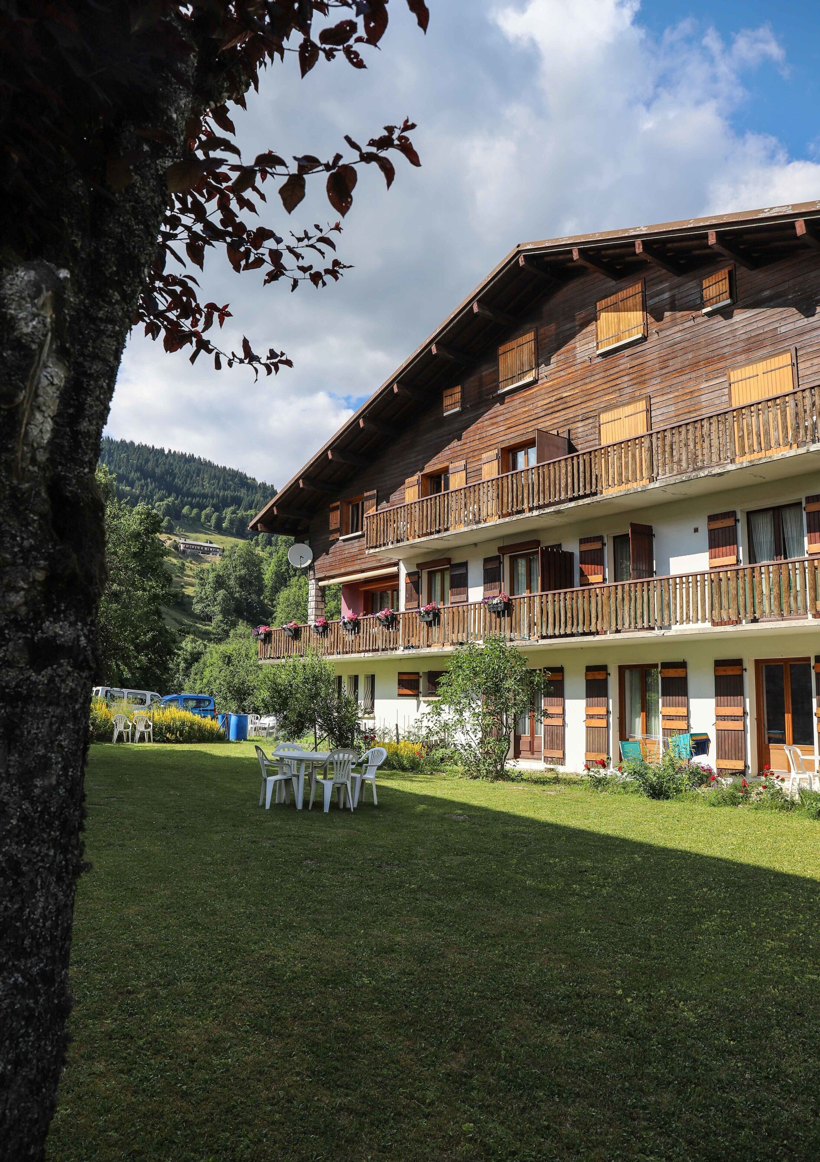 A multi-story hotel with balconies, a lawn, and a mountainous backdrop.