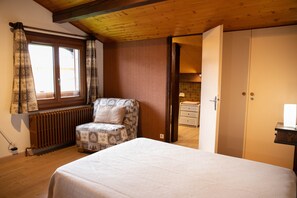 A bedroom with a bed, a chair, a wardrobe, and a window with curtains.