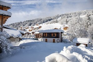 Un pueblo cubierto de nieve con edificios de madera, una pista de esquí al fondo y un cielo despejado.