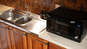 Een keuken met een dubbele spoelbak, een roestvrijstalen kraan, een zwarte magnetron en houten keukenkastjes.