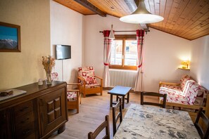 Um quarto aconchegante com teto de madeira, televisão na parede, sofá, mesa e uma cadeira.