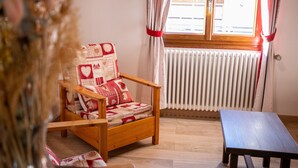 Ein Holzhocker mit gemustertem Kissen, ein Holztisch und ein Fenster mit Vorhängen.