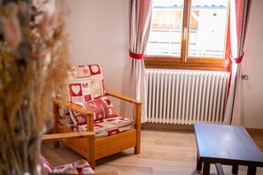 Une chaise en bois avec un coussin à motifs, une table en bois et une fenêtre avec des rideaux.
