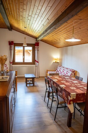 A cozy room with a wooden ceiling, a dining table with chairs, a bench, a radiator, and a window with curtains. - Apartment 'C4 - Chalet Tournier' with Mountain View, Shared Garden and Wi-Fi (Les Gets)
