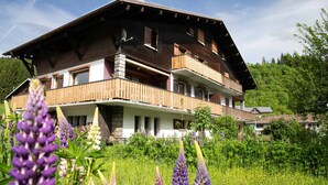 Eine mehrstöckige Holzhütte mit Balkonen, umgeben von üppiger Vegetation und blühenden Pflanzen.