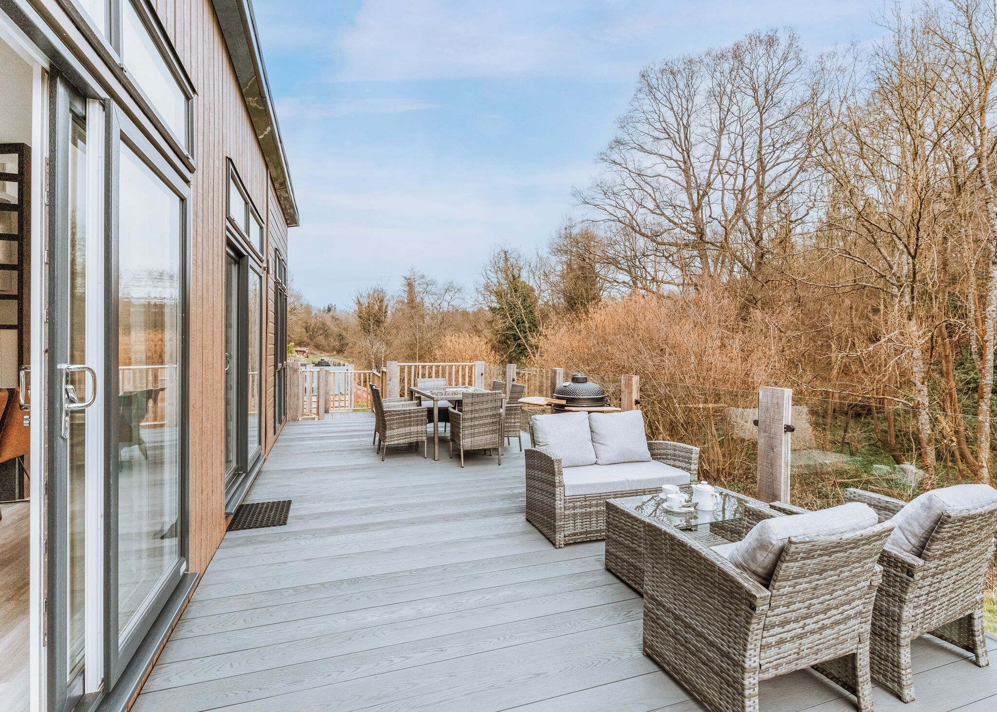 A deck with wicker furniture, a grill, and a glass door leading to a building.