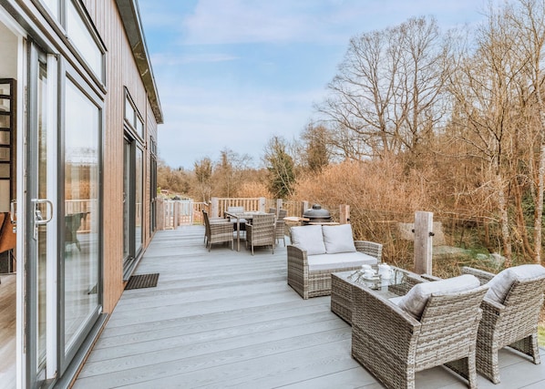 A deck with wicker furniture, a grill, and a glass door leading to a building.