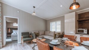 Un espace de vie moderne et bien éclairé, comprenant un canapé, une table à manger et des chaises, un coin cuisine et une vue dégagée sur l’extérieur grâce à une porte ouverte.