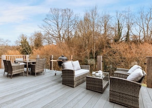 A deck with wicker furniture, a grill, and a glass table.