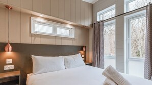 Un lit bien fait, avec du linge de lit blanc, une tête de lit, une table de chevet avec une lampe et une fenêtre avec des rideaux.