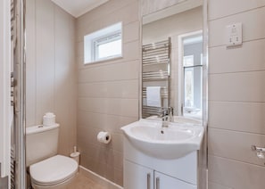 A bathroom with a toilet, a sink, a towel rack, and a window.