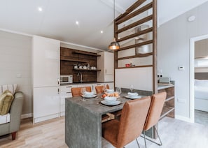 A modern kitchen with a central island, dining area with chairs, and a visible microwave.