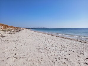 Une vaste plage de sable fin, sous un ciel dégagé et une mer calme.