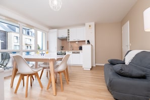 A modern kitchen with white cabinets, a dining table with chairs, and a black sofa.