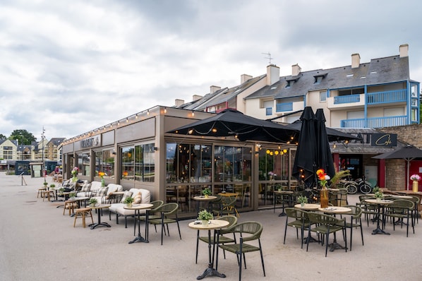An outdoor café with tables and chairs, a glass storefront, and a building with blue balconies.