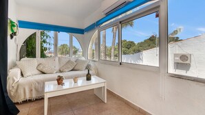 A room with a white sofa, a white coffee table, and large windows with a view of trees and buildings. - Apartment 'La Finca' with Sea View, Wi-Fi and Air Conditioning (Teulada)