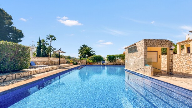 A clear swimming pool with stone walls and a tiled deck, surrounded by greenery and a clear sky. - Apartment 'La Finca' with Sea View, Wi-Fi and Air Conditioning (Teulada)