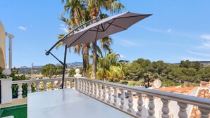 A balcony with a white table, a white balustrade, and a view of trees and distant hills. - Apartment 'La Finca' with Sea View, Wi-Fi and Air Conditioning (Teulada)