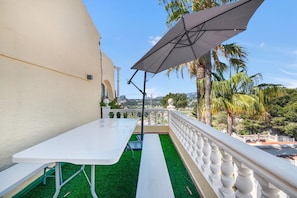 A balcony with a white table and bench, a white railing, and a view of palm trees and distant buildings. - Apartment 'La Finca' with Sea View, Wi-Fi and Air Conditioning (Teulada)