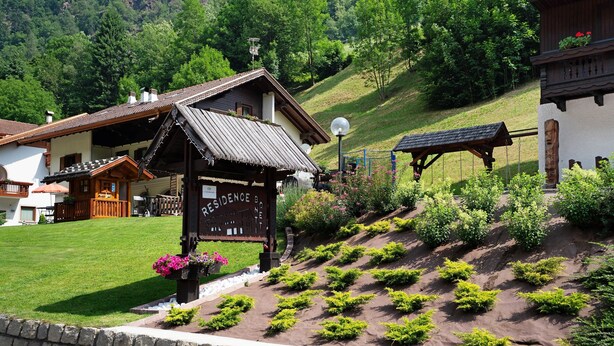 A traditional chalet with a wooden exterior, a signboard, and a well-maintained garden with shrubs and flowers.