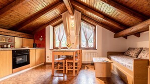 A cozy kitchen with wooden cabinets, a dining table, and a sofa in a loft-style room with exposed wooden beams.